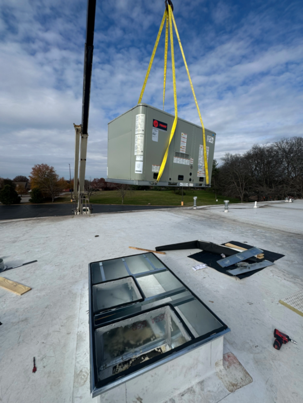 Commercial rooftop HVAC unit being lifted by crane onto a flat roof