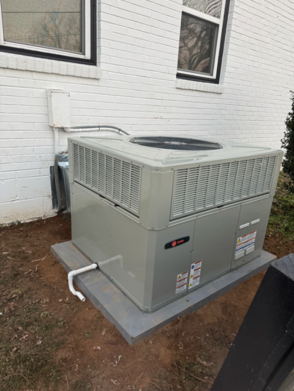 Large package HVAC unit installed on a slab beside a white brick home