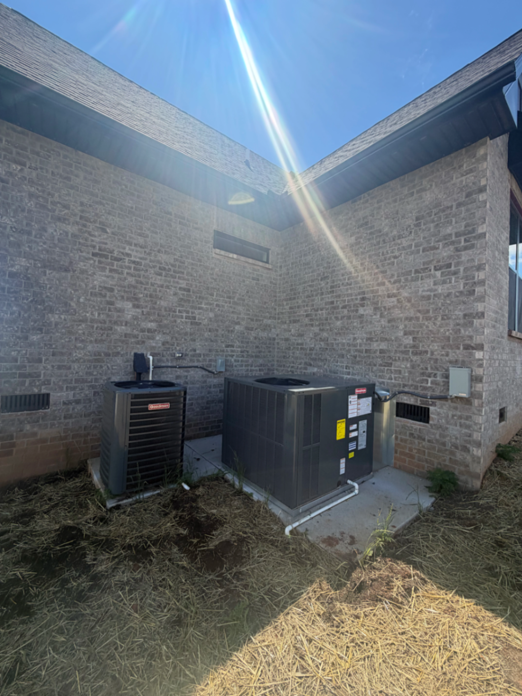 Two outdoor HVAC condenser units installed beside a brick home on separate concrete pads