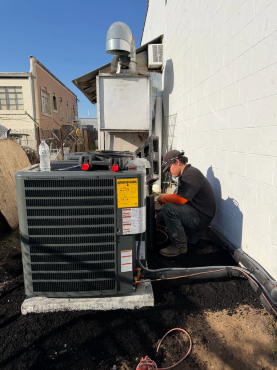 HVAC technician working beside a newly installed outdoor condensing unit at a commercial site